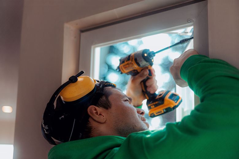 A SilverLine installer drilling a new window frame into place, ear defenders on