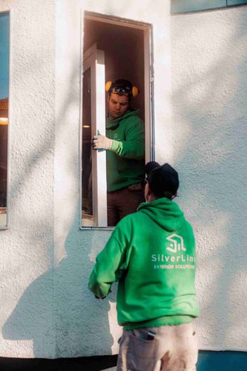 Two SilverLine installers passing a new window unit through the opening